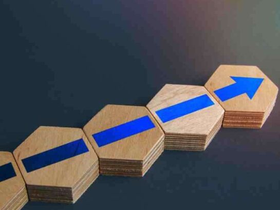 Wooden Blocks With Blue Arrows Forming A Rising Diagonal Line On A Gray Background, Symbolizing Growth Or Progress.