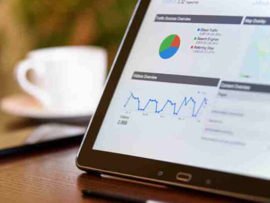 Tablet Displaying Graphs And Data Analysis On Screen, Placed On A Wooden Table Next To A Coffee Cup.