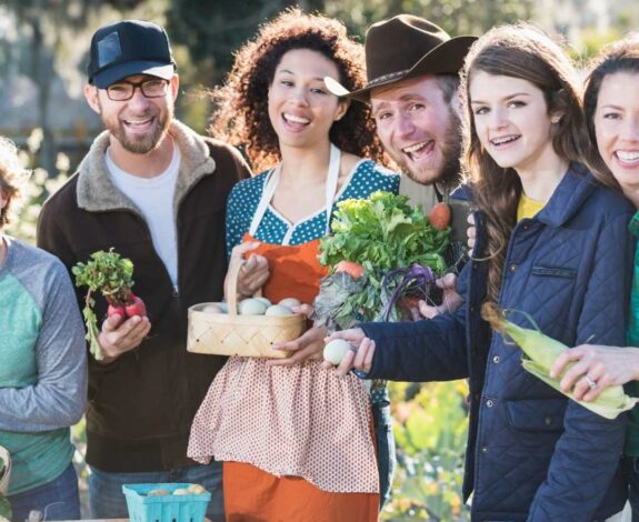 A Group Of Happy Adults Holding Fresh Vegetables And Eggs At A Sunny Outdoor Farmers Market.