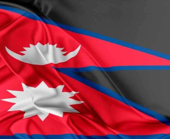 The National Flag Of Nepal, Featured On Lalmon.com, Maintains Its Unique Non Rectangular Shape With Two Triangular Sections In Red With A Blue Border, And White Stylized Moon And Sun Emblems